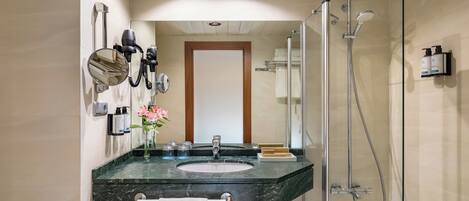 Un baño moderno con lavamanos de mármol, cabina de ducha con mampara de vidrio y espejo con secador de pelo.