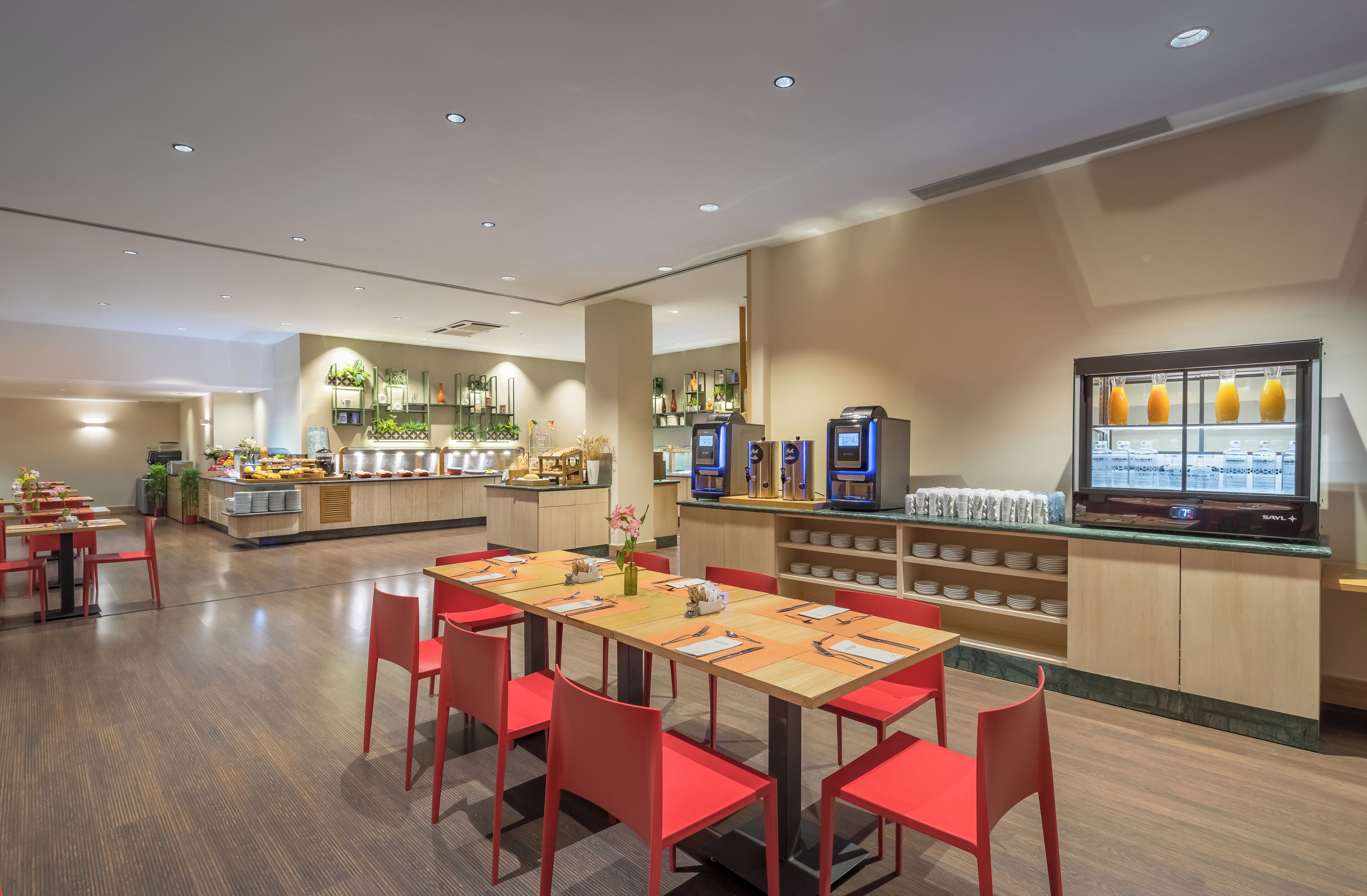 A modern restaurant with wooden tables and red chairs, a buffet area, and a coffee machine.