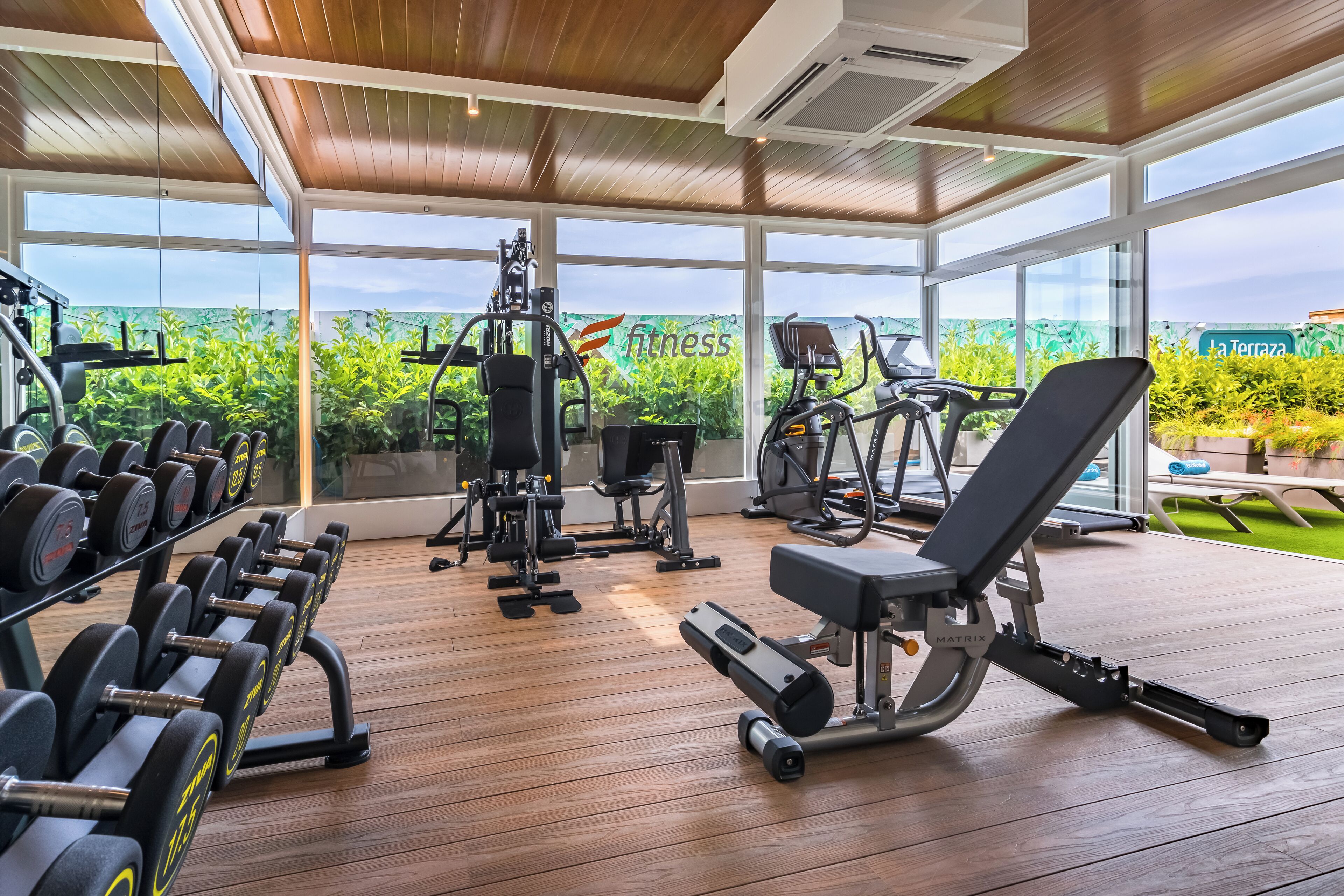 A gym with exercise equipment, large windows, and a view of greenery.
