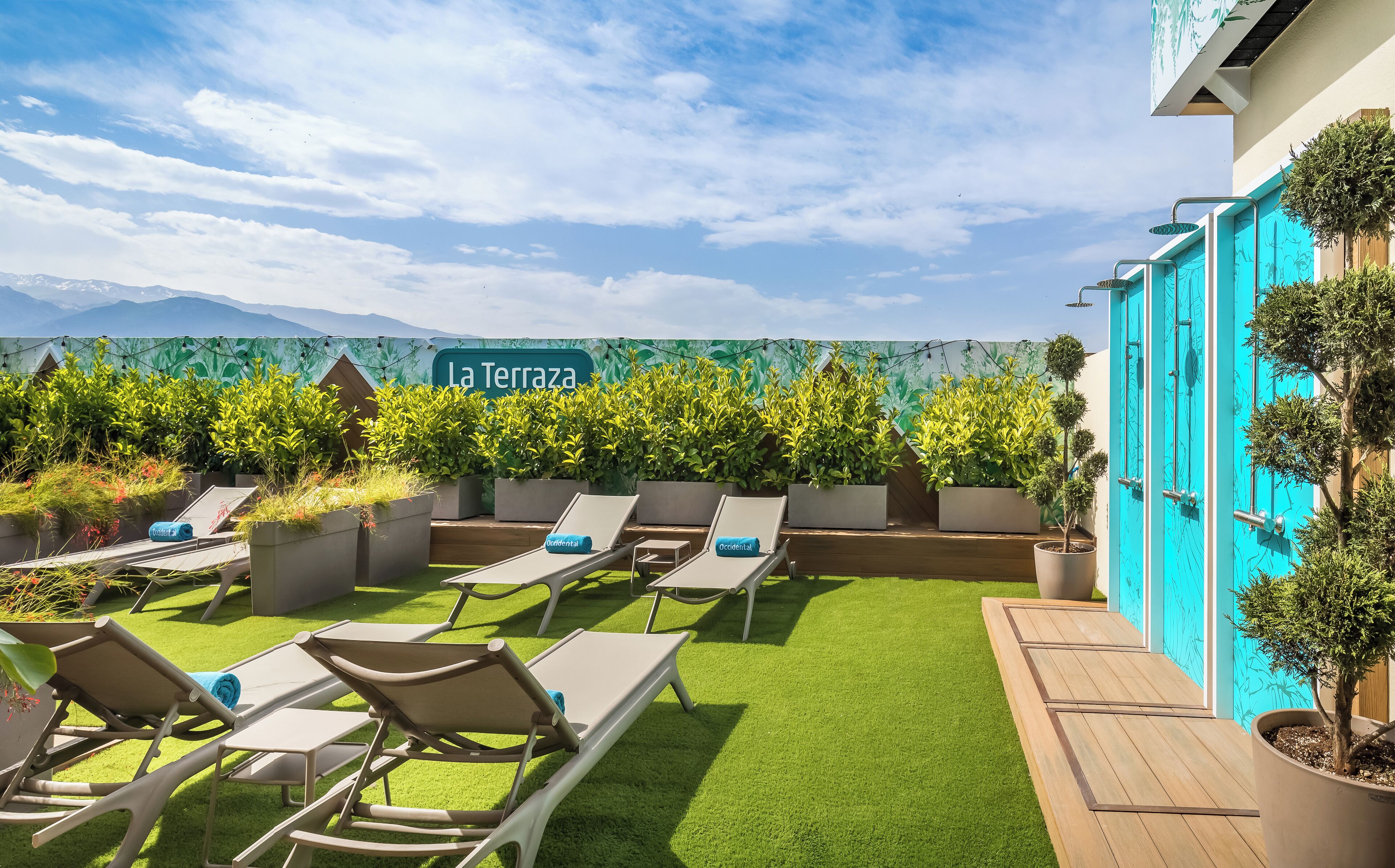 Une terrasse sur le toit, dotée de chaises longues, un panneau indiquant « La Terrazas », et une vue sur les montagnes.