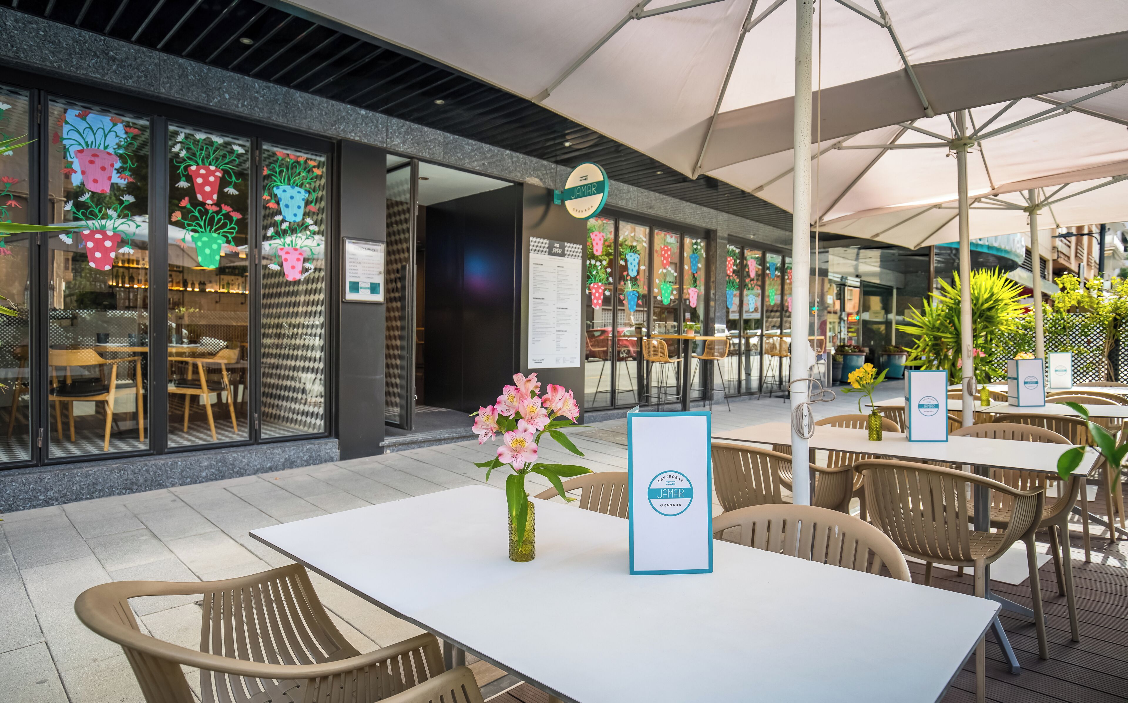 An outdoor seating area with tables and chairs, a sign for 'JAMAR', and a menu board.