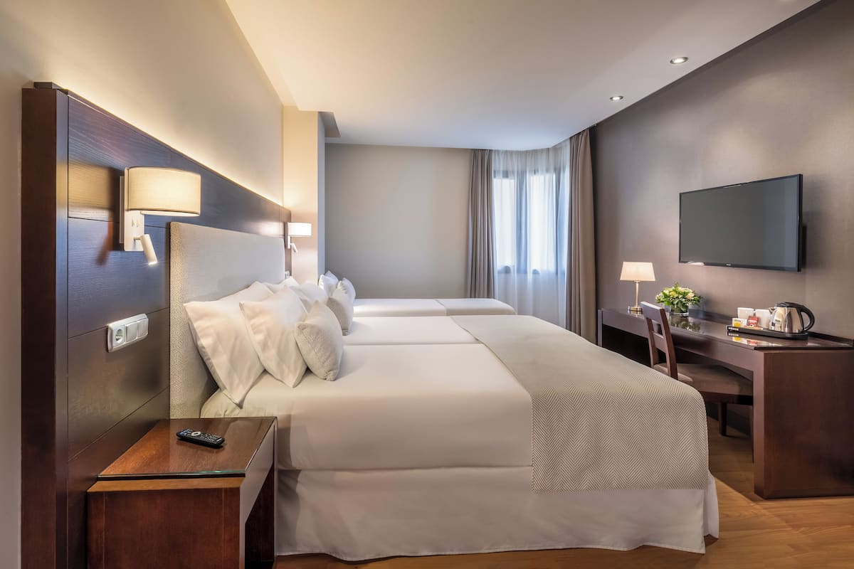 Une chambre d’hôtel avec deux lits, un bureau, une télévision et une fenêtre avec des rideaux.