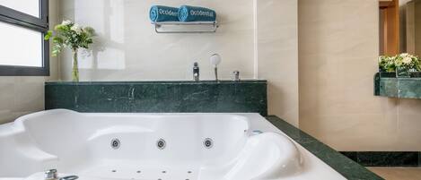 A modern bathroom with a large white bathtub, a marble countertop, a towel rack with folded towels, a vase with flowers, and a mirror.