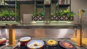 Een ontbijtbuffet met diverse gerechten, waaronder eieren, omelet en bacon, op een roestvrijstalen toonbank.
