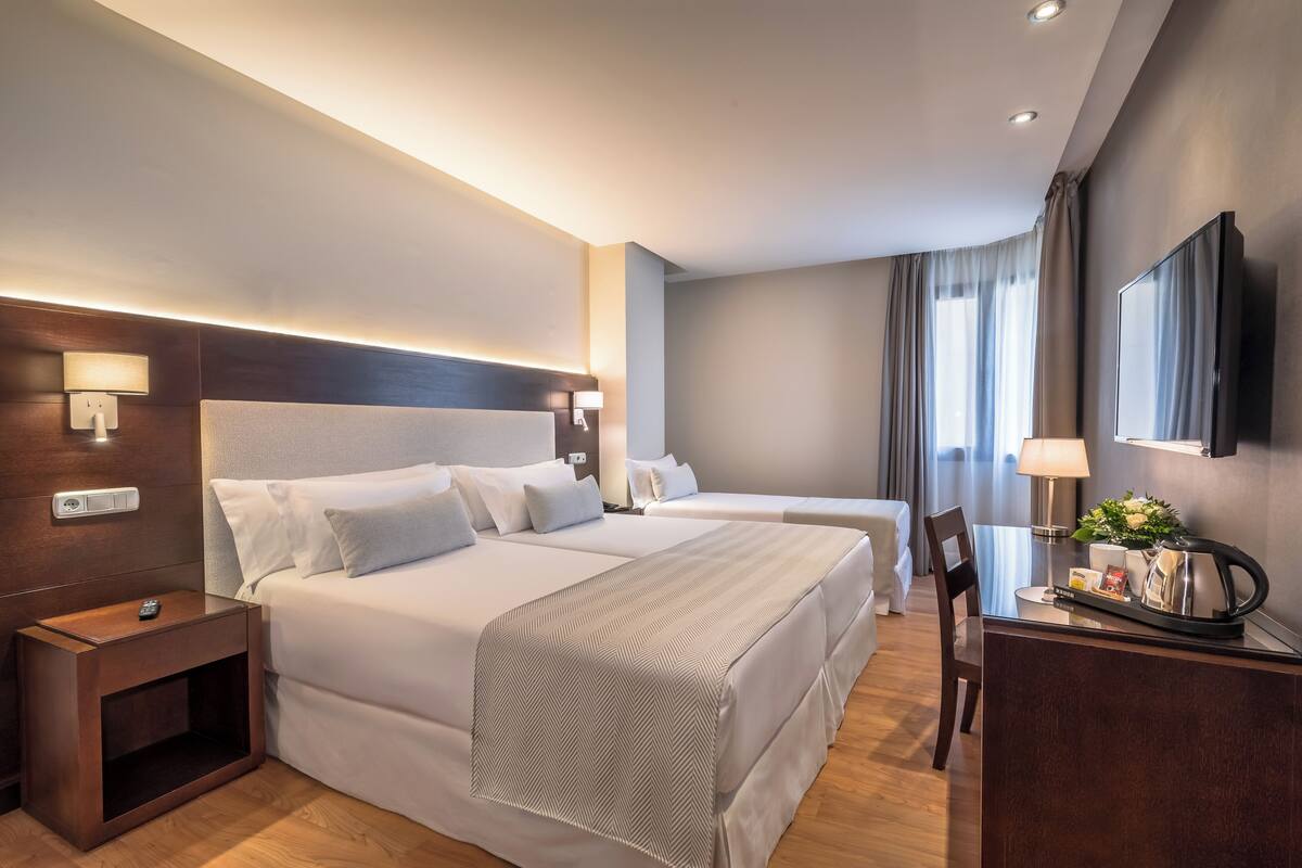 Une chambre d’hôtel avec deux lits, un bureau avec une chaise, une télévision et une table de chevet avec une lampe.