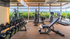 Een sportschool met diverse fitnessapparatuur, waaronder gewichten, banken en cardioapparaten, met grote ramen met uitzicht op groen.