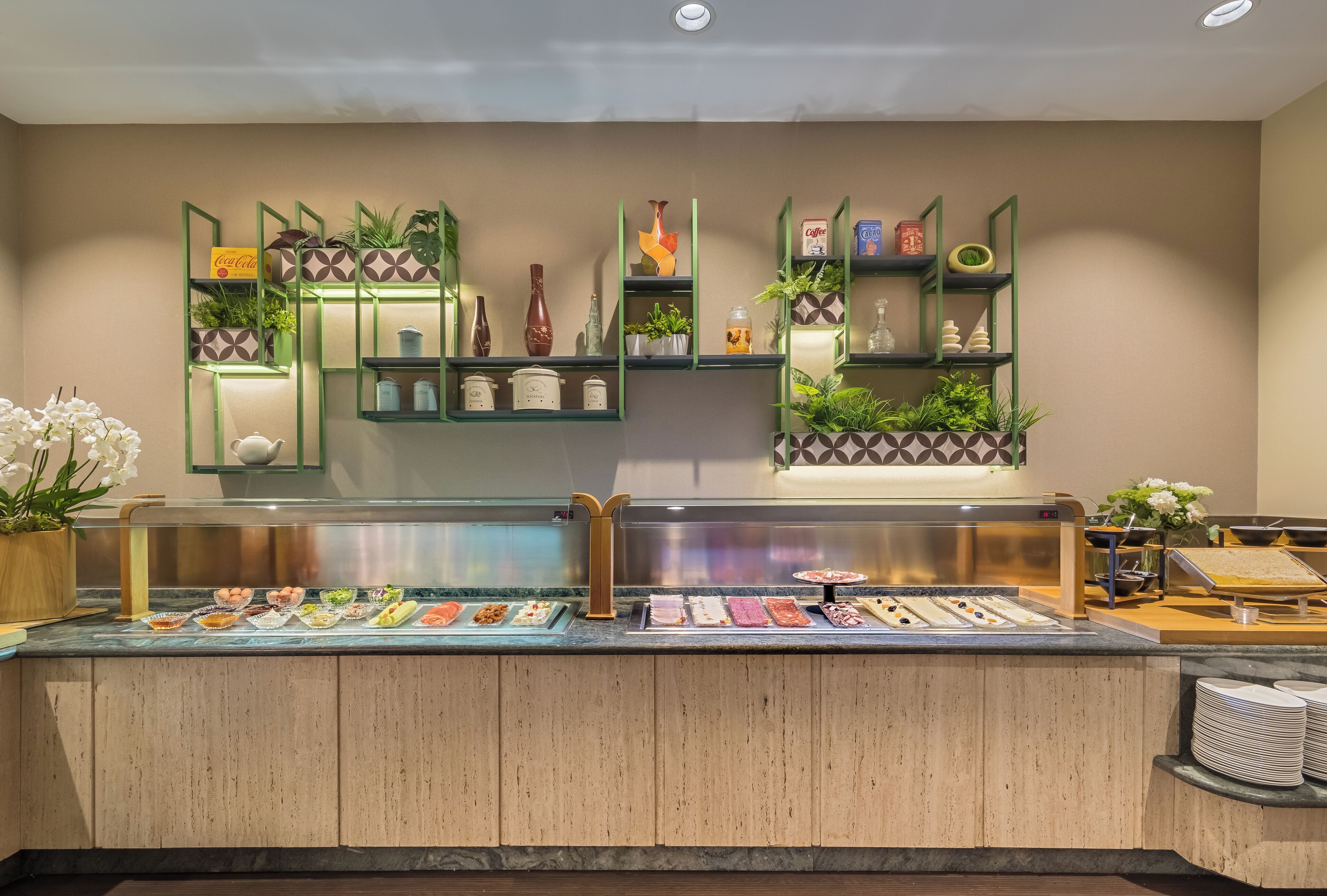 Un mostrador de buffet con diversos alimentos y una pared decorativa con estantes y plantas.