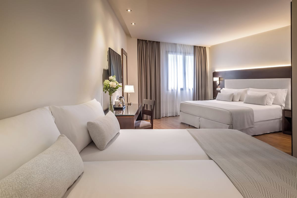 Une chambre d’hôtel avec un grand lit, un lit plus petit, un bureau avec une lampe et une chaise.