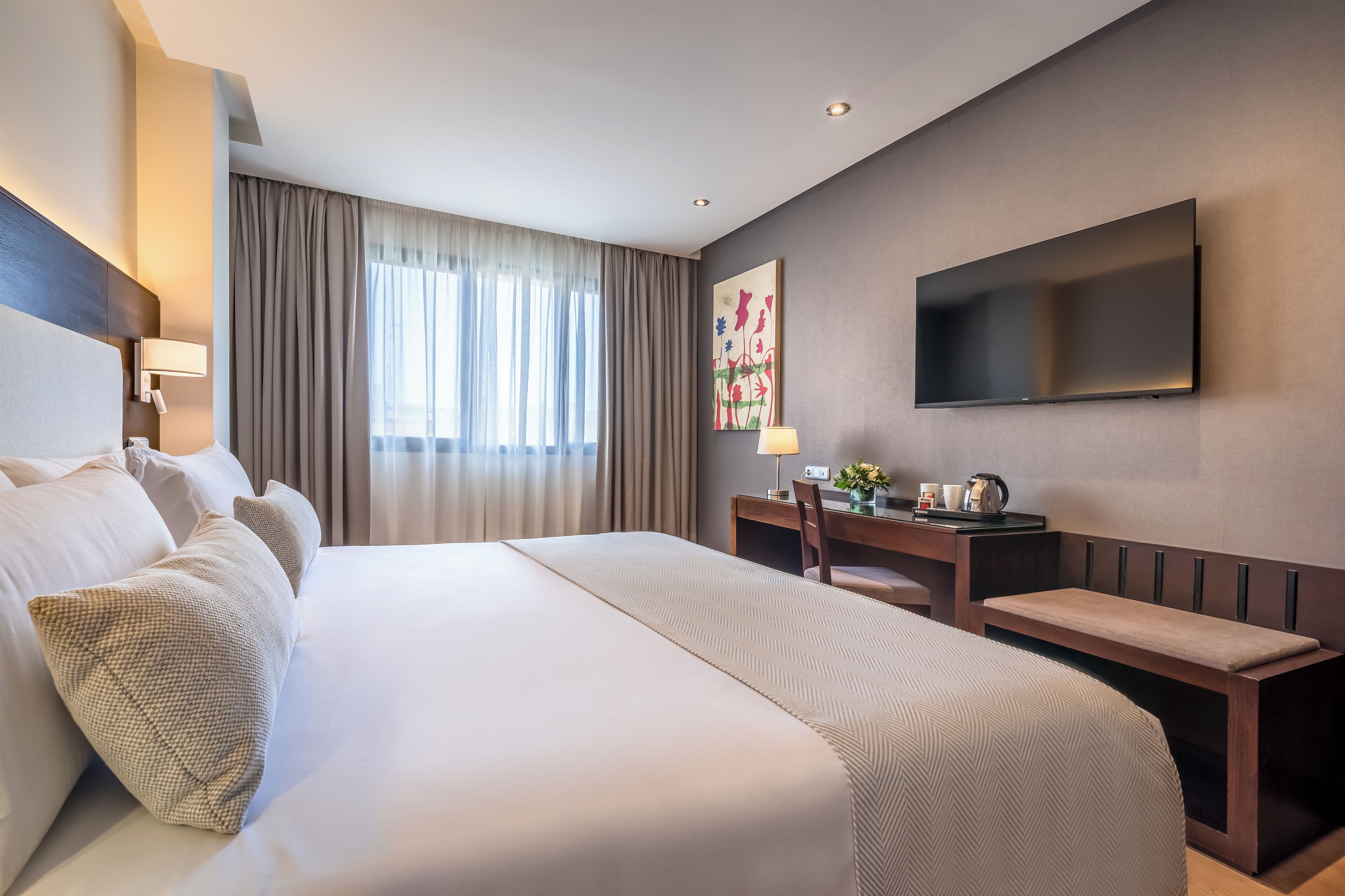 Een hotelkamer met een groot bed, een bureau met stoel, een flatscreen televisie aan de muur en een raam met gordijnen.