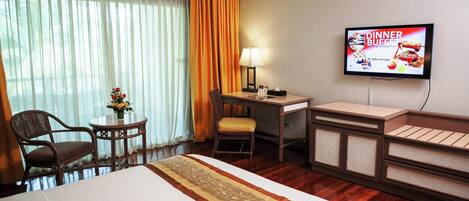 Habitación de hotel con una cama, un escritorio con lámpara, un televisor y una pequeña mesa con flores.