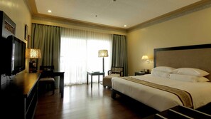 A hotel room with a large bed, a desk with a television, a lamp, and a chair.