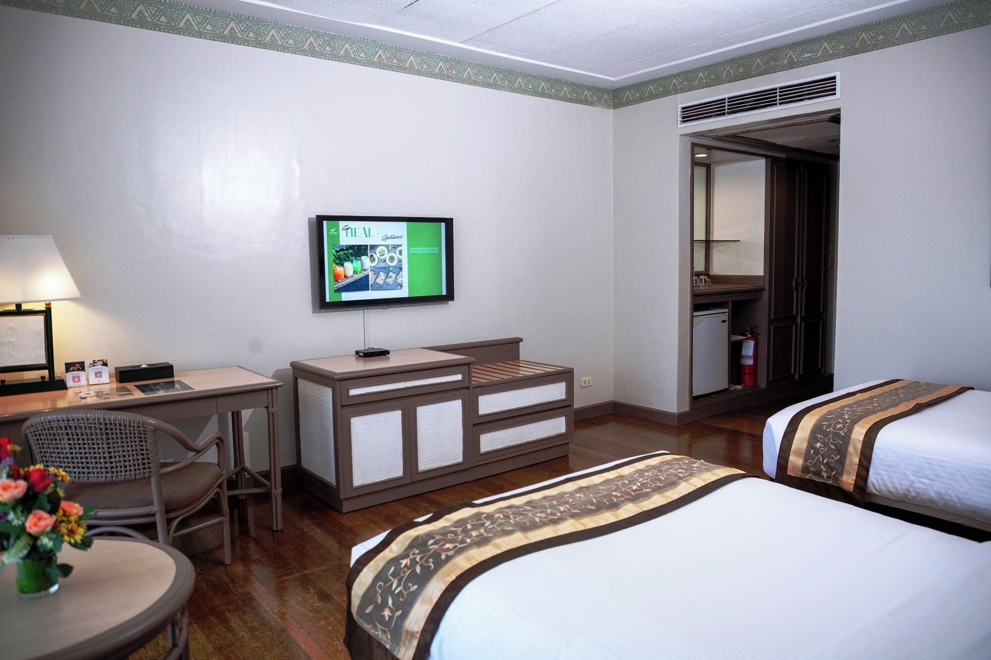 A hotel room with a desk, chair, TV, dresser, and two beds.