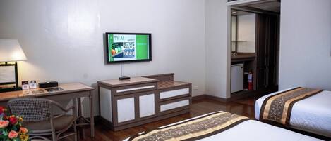 A hotel room with a desk, chair, TV, dresser, and two beds.
