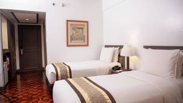 Habitación de hotel con dos camas, piso de madera, un cuadro en la pared y una mesita de noche con una lámpara.