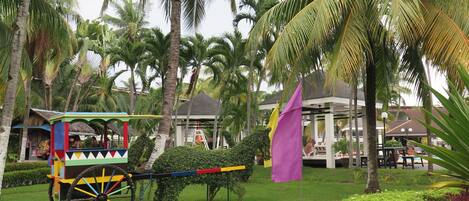 Un carro colorido en un jardín exuberante con palmeras y una bandera morada.