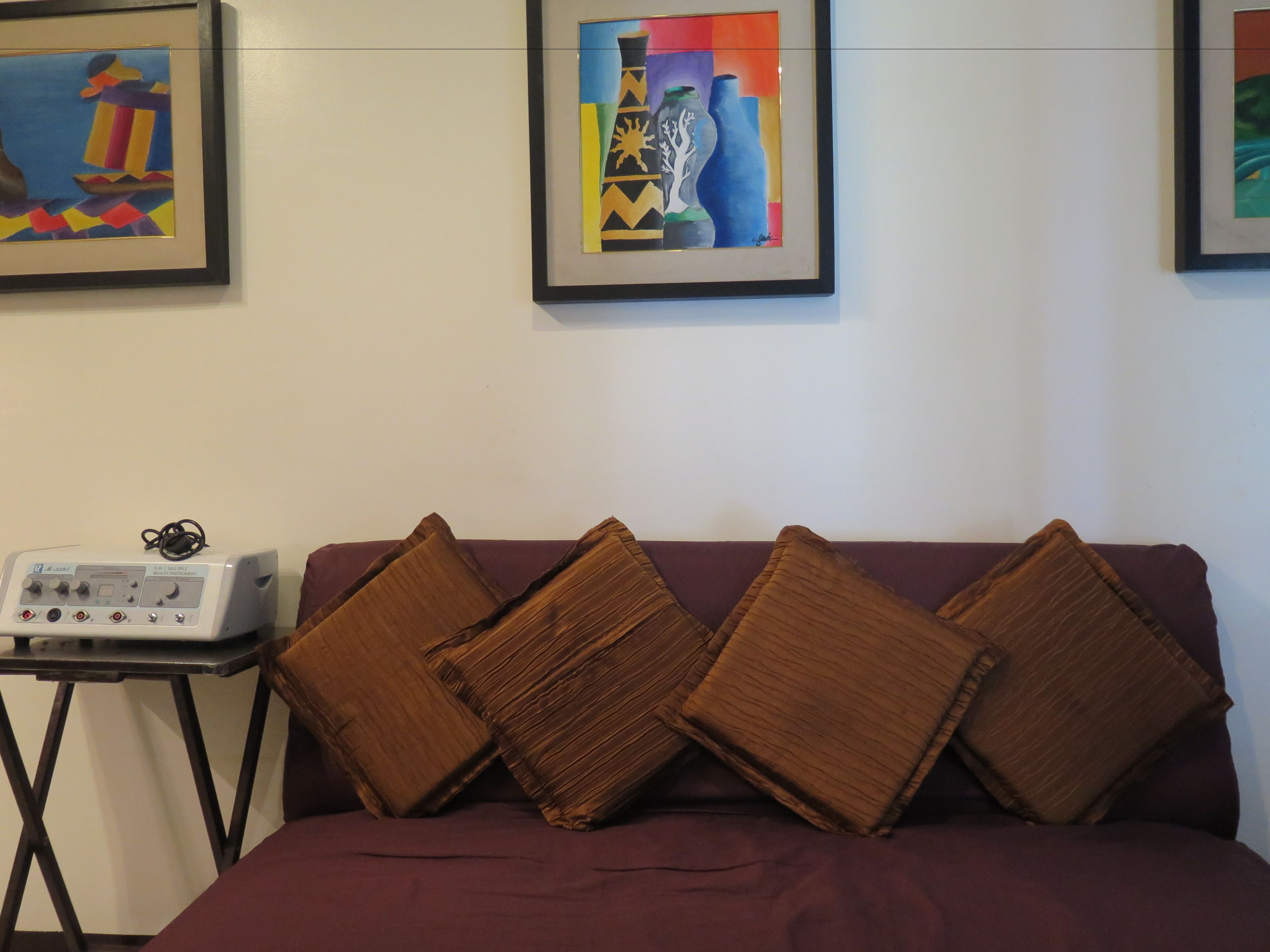 A room with a bed, a table with a device, and two framed artworks on the wall.