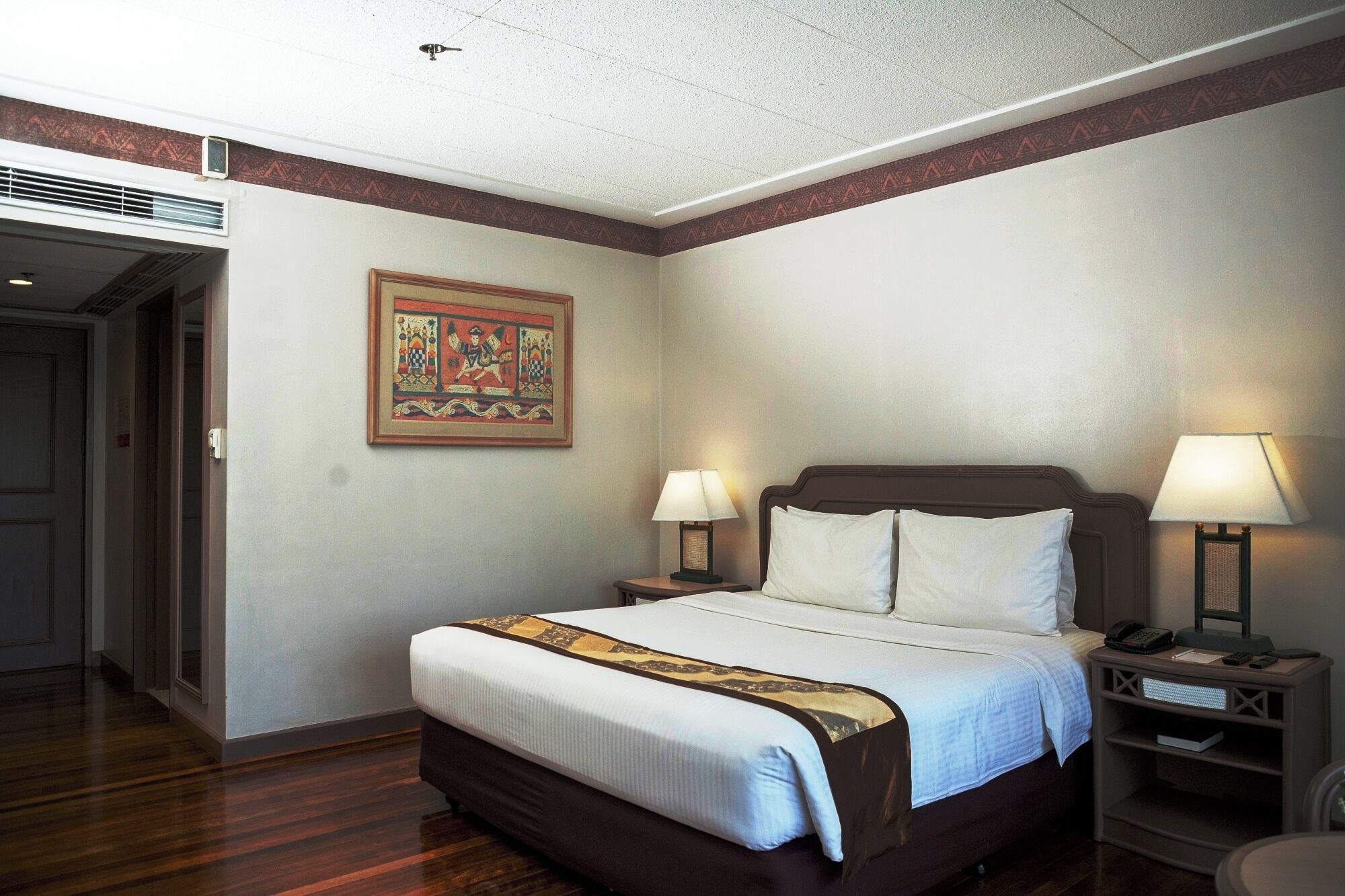 A hotel room with a bed, two bedside lamps, a nightstand, and a decorative wall hanging.