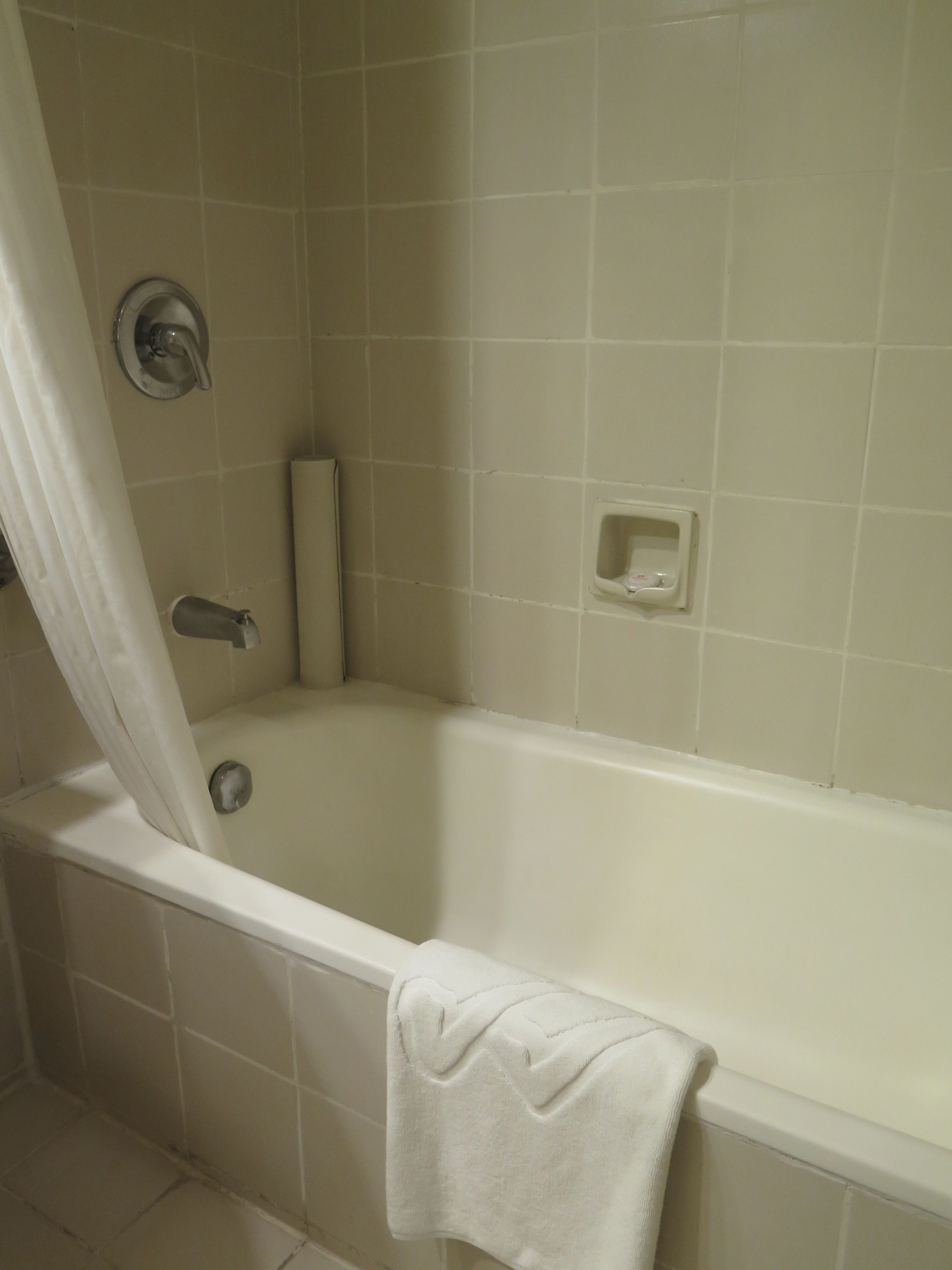 A bathroom with a bathtub, a shower curtain, a towel, and a soap dish.