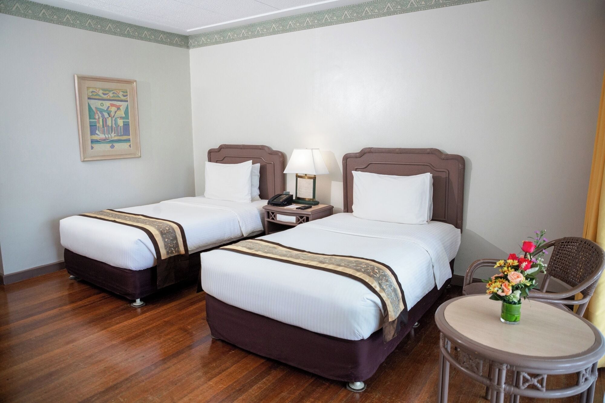 Habitación de hotel con dos camas, una mesita con un florero y una silla.