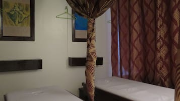 Two single beds with white mattresses, adorned with framed artworks above, and a patterned curtain filtering the light.