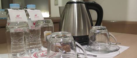 A table with water bottles, a glass carafe, a glass teapot, and a coffee pot, all on a white placemat with a logo.
