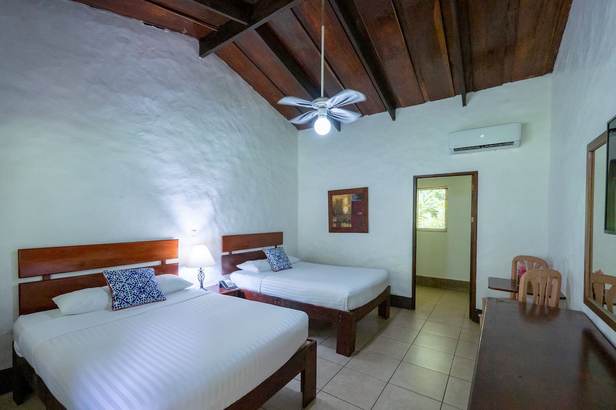 Une chambre avec deux lits, un ventilateur de plafond, un appareil de climatisation et une petite table avec des chaises.