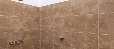A shower with brown tiles and a handheld showerhead.