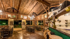 A rustic wooden interior with dining tables and chairs, a ceiling fan, and a green counter with a sink. - Villa Lapas Jungle Village (Tárcoles)