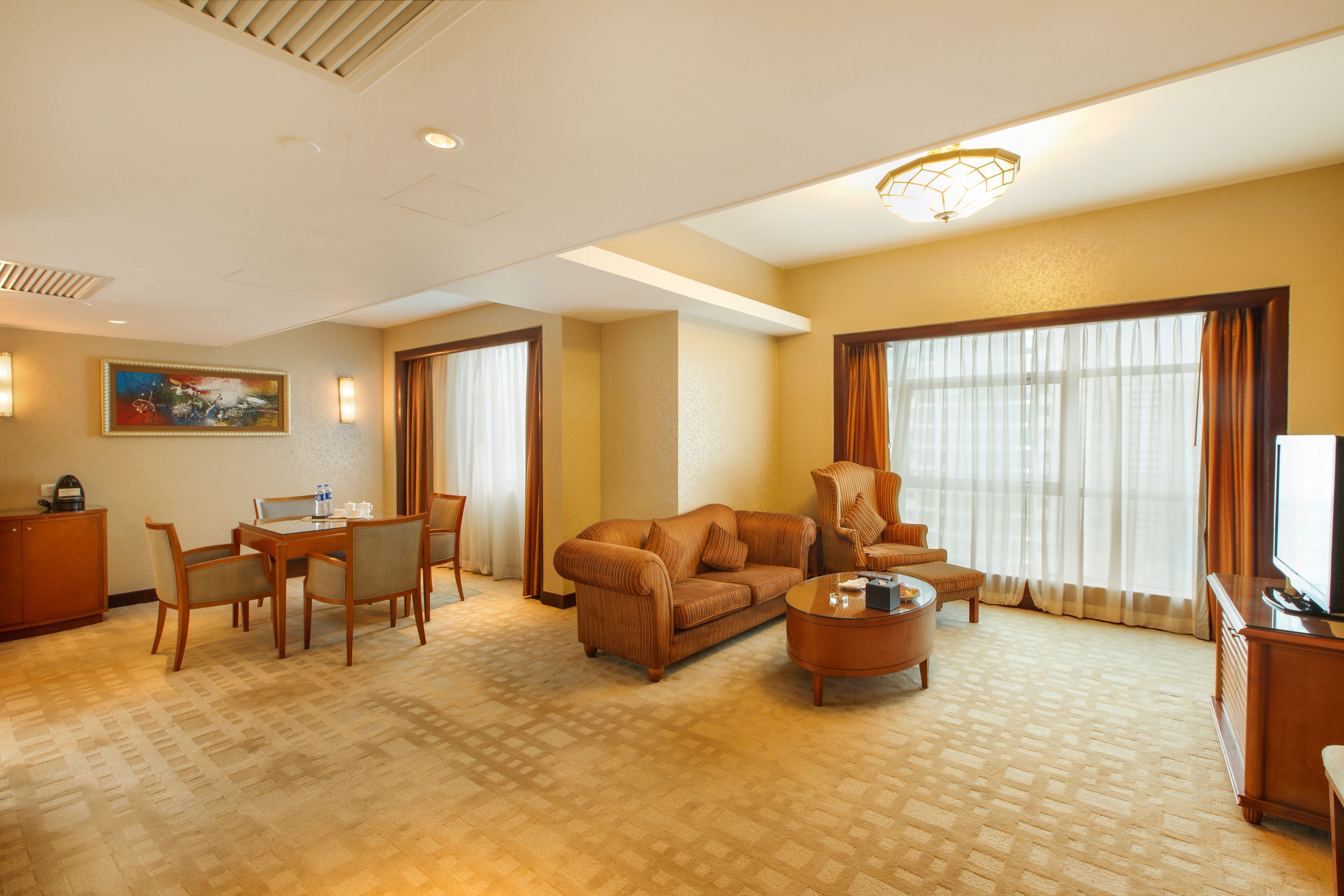 A hotel room with a living area featuring a sofa, armchair, coffee table, dining table with chairs, and a television.