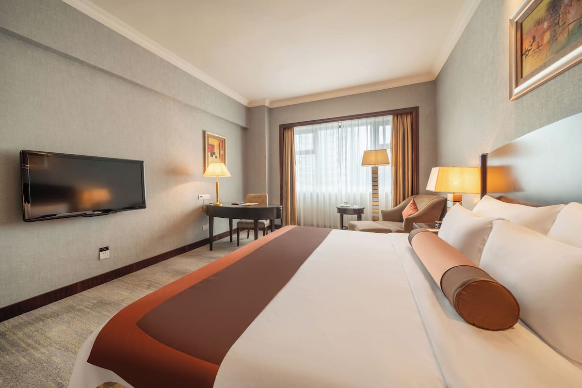 Ein Hotelzimmer mit einem Bett, einem Schreibtisch, einem Sessel, einem Fernseher und einem Vorhangfenster.