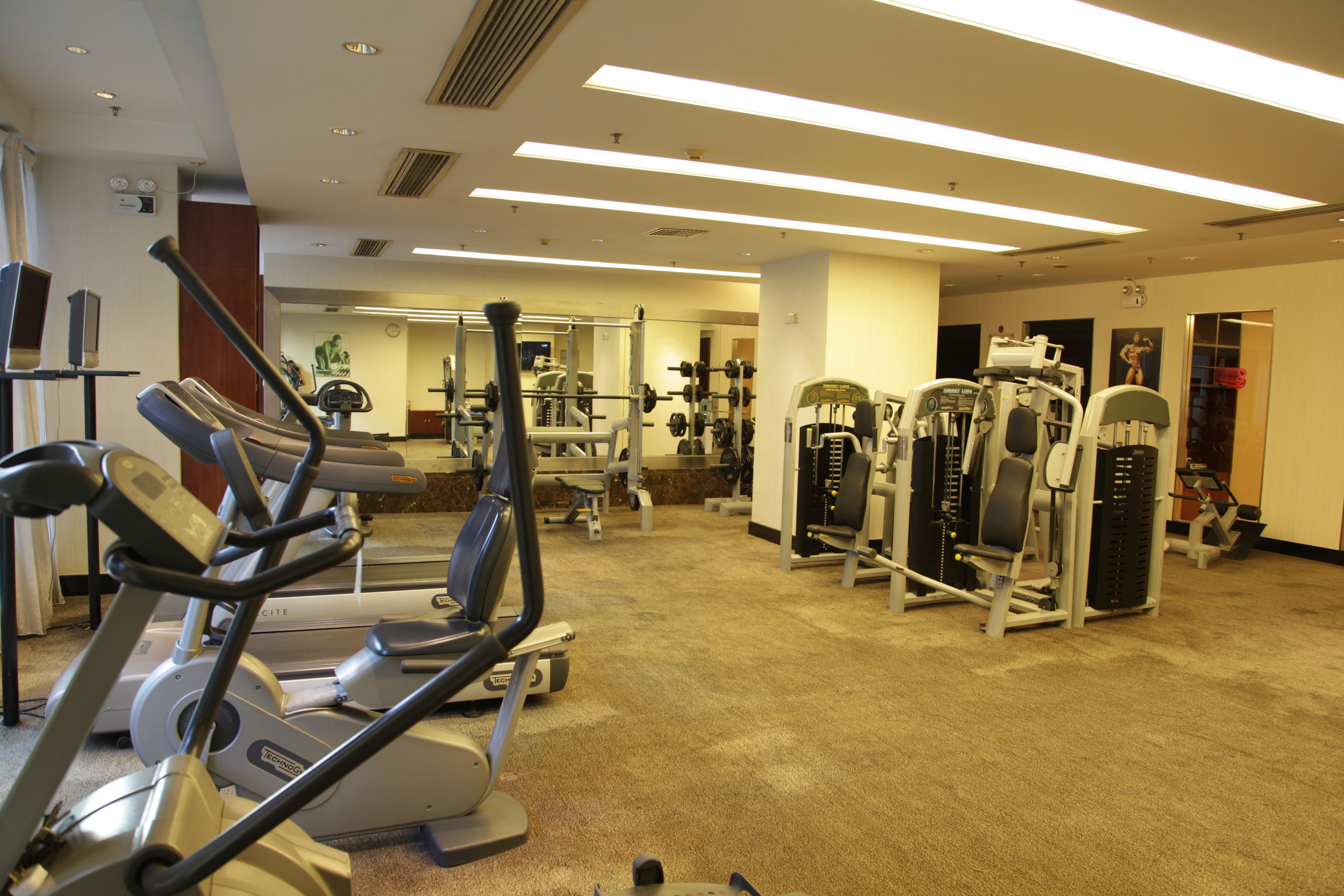 Une salle de sport équipée de tapis de course, d’appareils de musculation et d’un miroir.