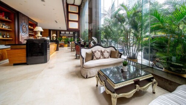 A spacious lobby with a high ceiling, a coffee bar, seating area, and a view of palm trees through large windows. - Guangzhou Grand International Hotel (Guangzhou)