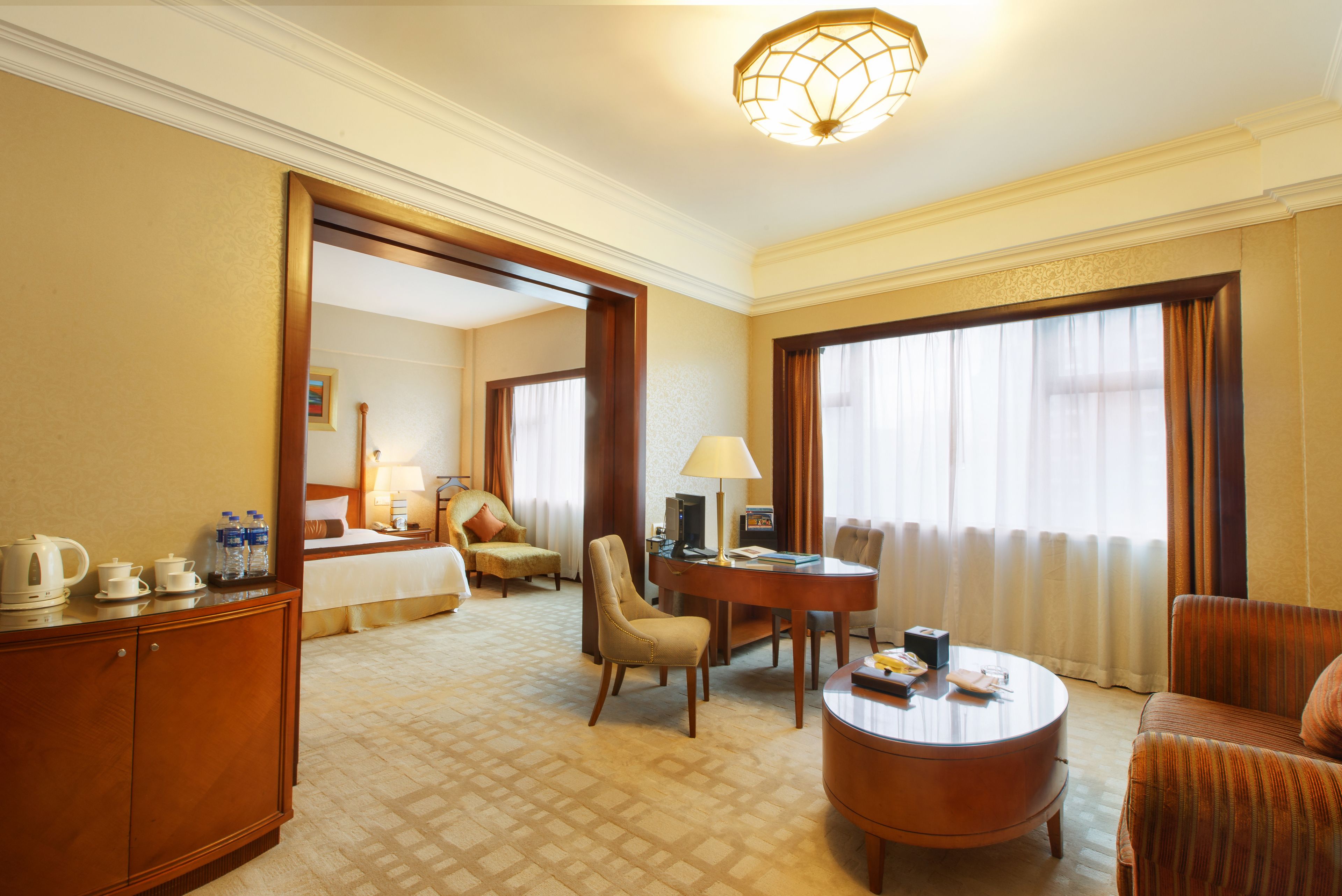 A hotel room with a bed, a sitting area with a table and chairs, a small kitchenette, and a large window with curtains.