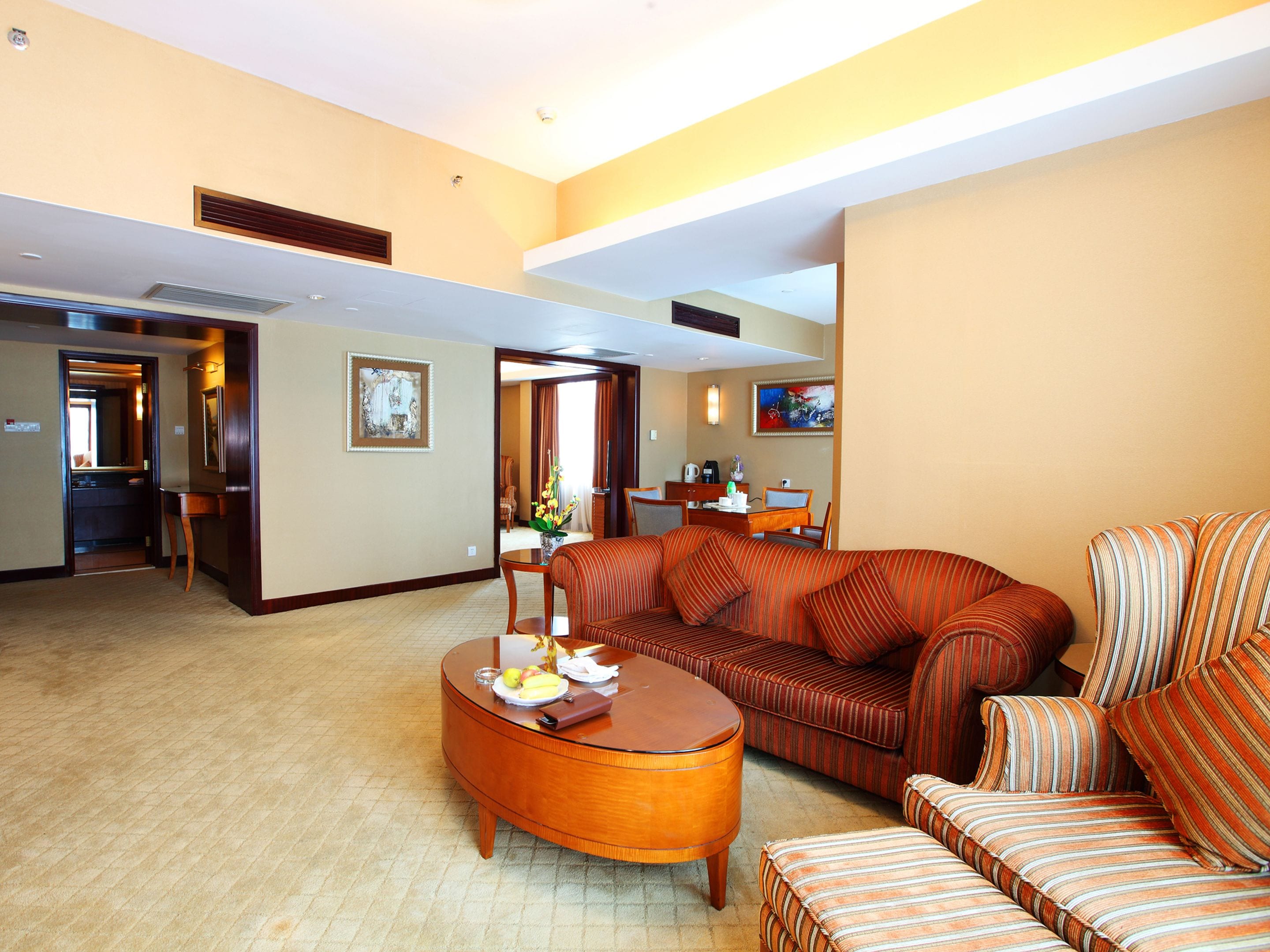 Habitación de hotel con sala de estar que incluye un sofá, una mesa de centro de madera y una mesa de comedor con sillas.