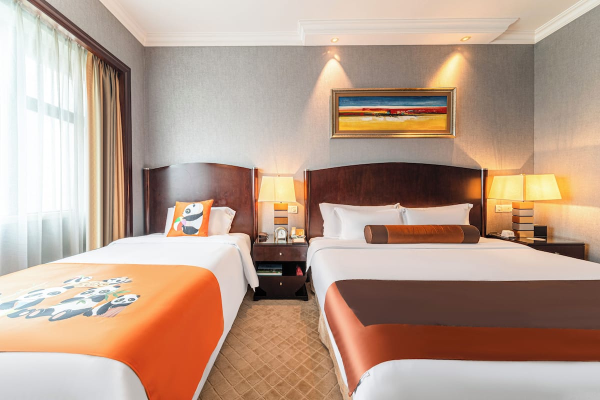 Ein Hotelzimmer mit zwei Betten, einem Bild an der Wand und einem Fenster mit Vorhängen.
