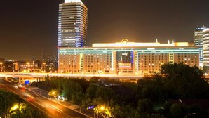 A multi-story hotel with a prominent horizontal marquee and a tall building with illuminated windows in the background. - Gubei Garden Hotel (Shanghai)