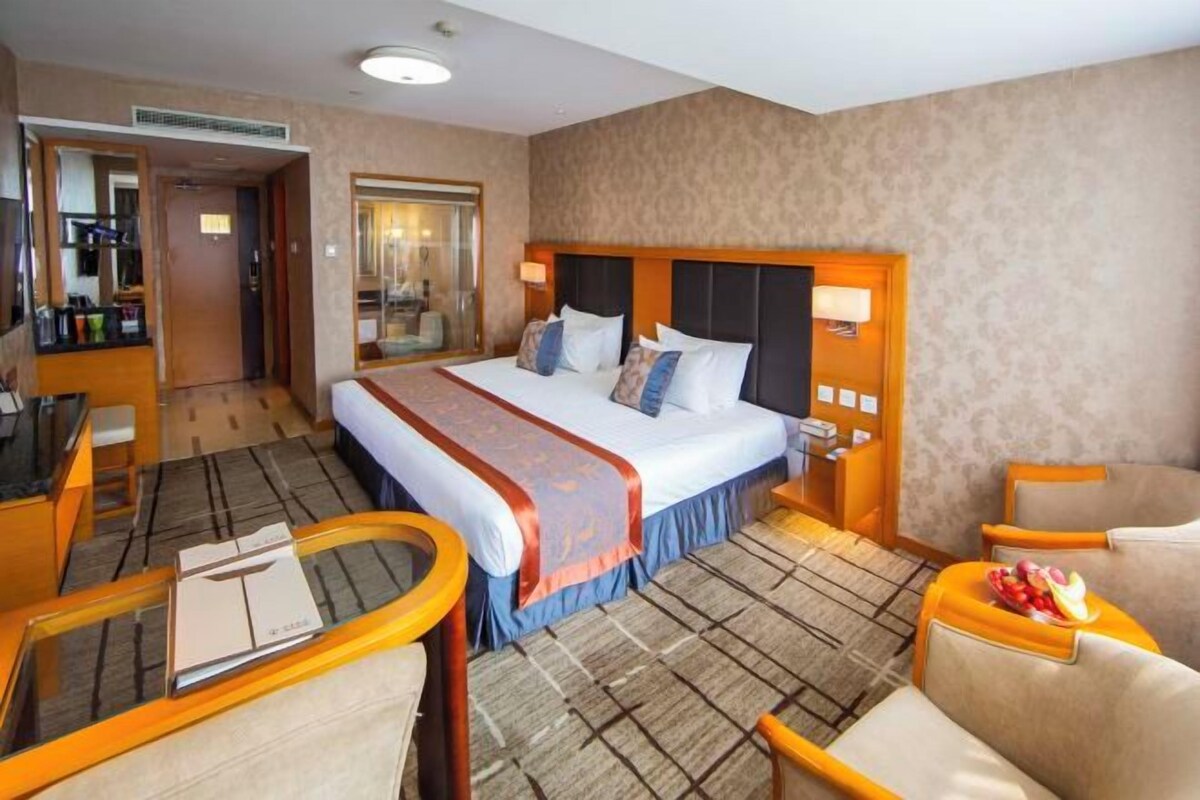 A hotel room with a large bed, a desk with a chair, a small table, and a sofa.
