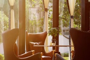 A room with a table and chairs, a potted plant, and large windows with a view of greenery. - Shanxi Grand Hotel (Taiyuan)