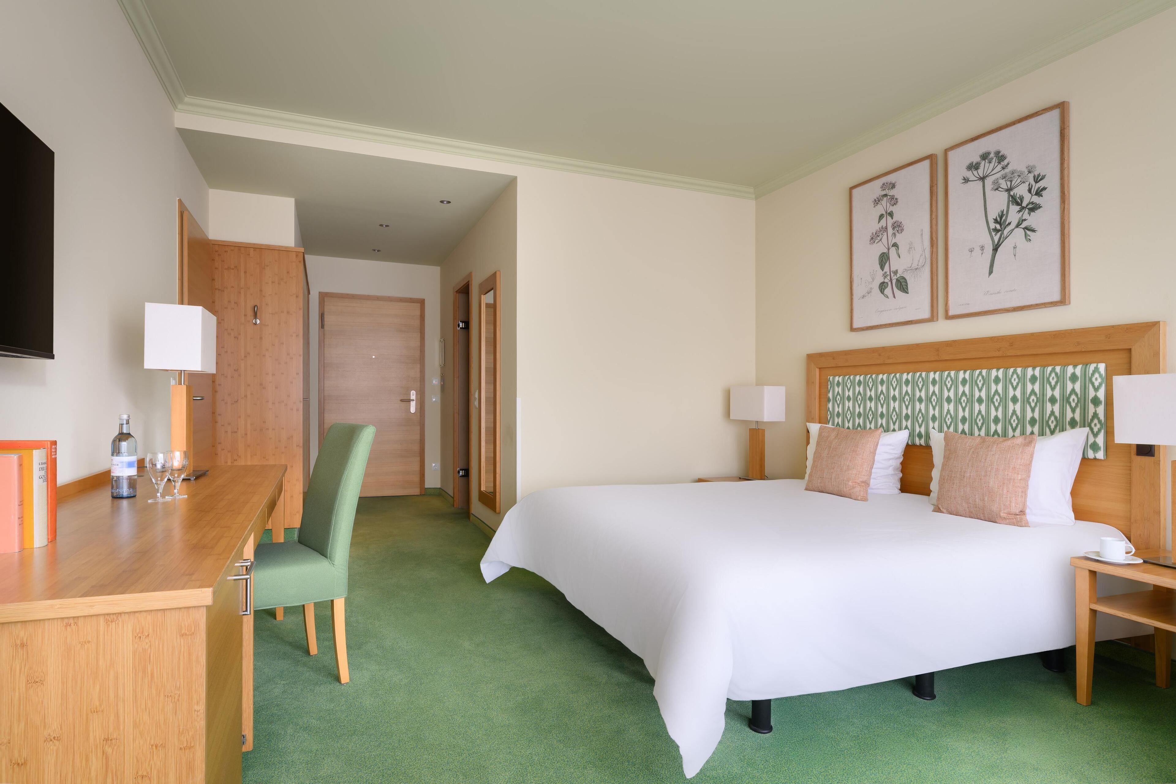 Una habitación de hotel con una cama grande, un escritorio con silla, una mesita de noche y un televisor montado en la pared.
