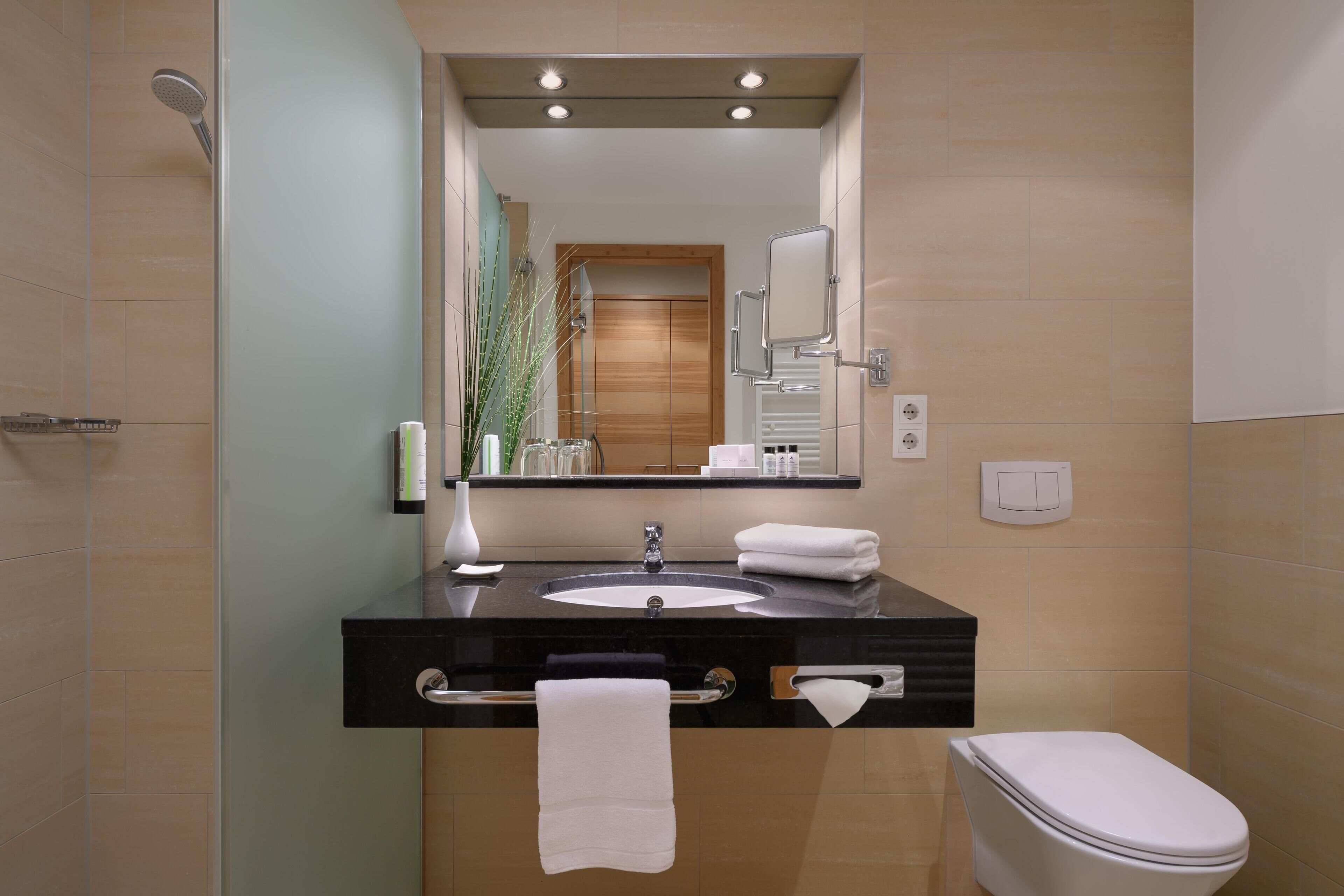 Un baño moderno con un lavamanos negro, inodoro blanco y un espejo grande sobre el lavamanos.