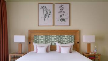 A neatly made double bed with white and pink pillows, a wooden headboard with a patterned wallpaper, and two bedside tables with lamps and books.