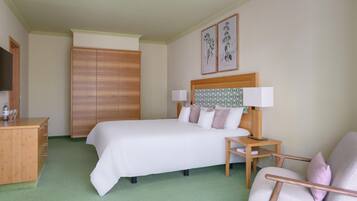 A hotel room with a bed, a wooden wardrobe, a desk with a lamp, and a chair.