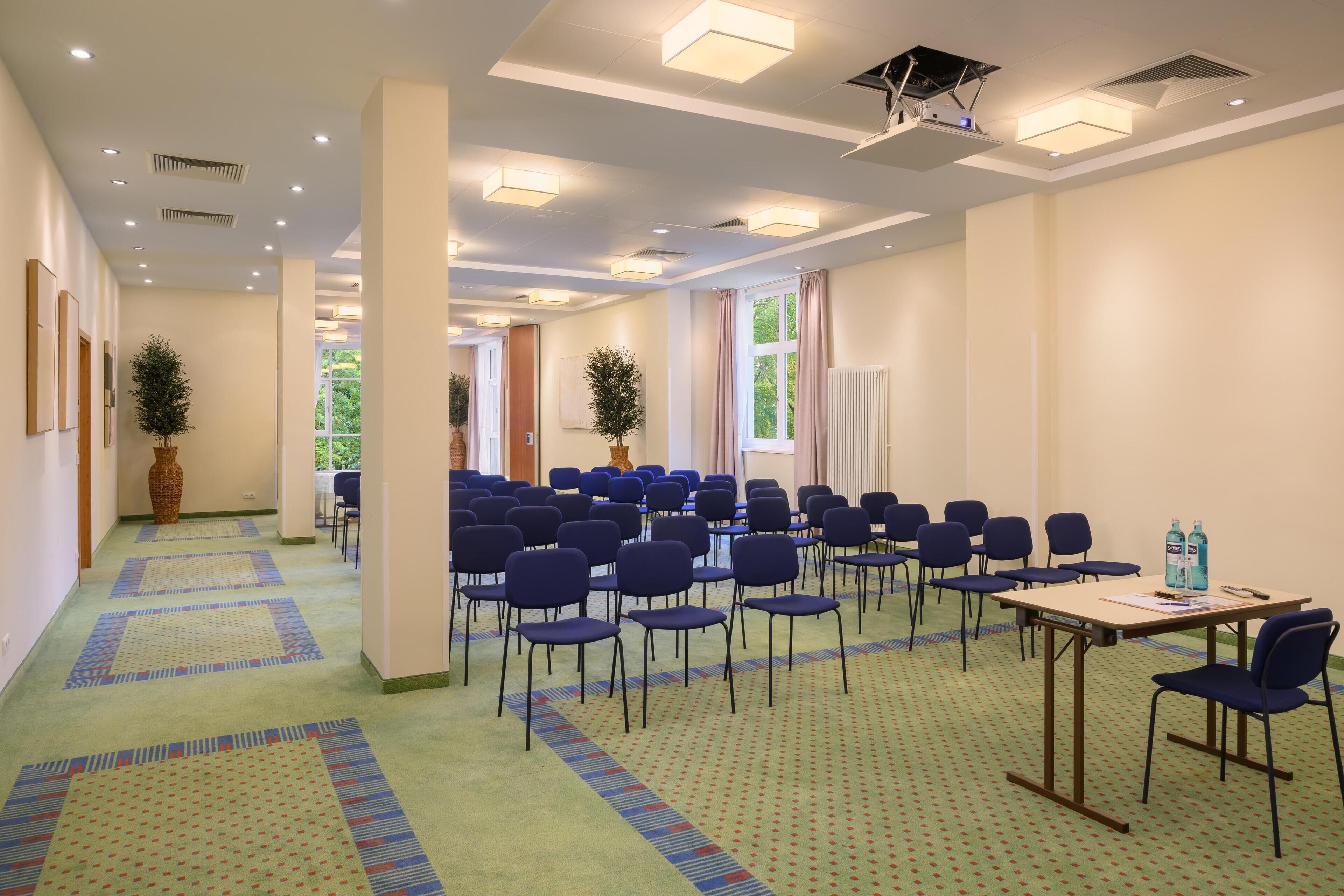 A conference room with rows of chairs, a table with a projector, and a carpeted floor.
