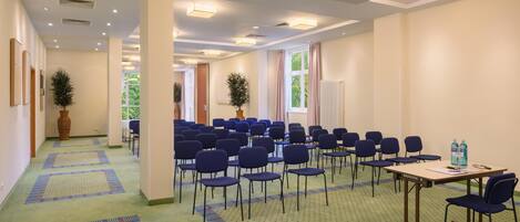 A conference room with rows of chairs, a table with a projector, and a carpeted floor.