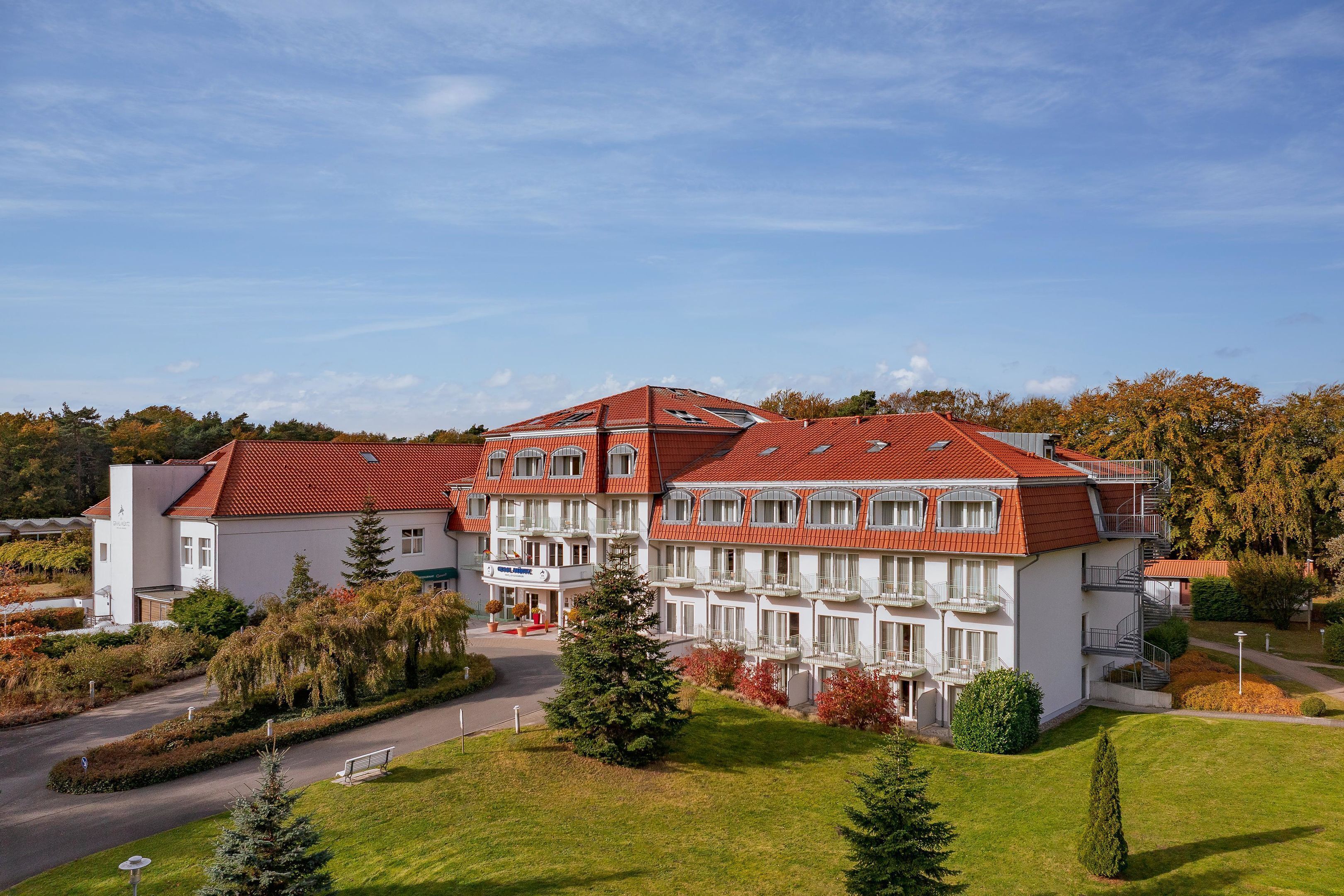 Ein großes Hotel mit mehreren Etagen, einem roten Ziegeldach und einem gepflegten Garten.