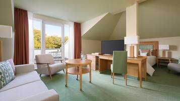 A hotel room with a sofa, two armchairs, a desk, a television, and a balcony with curtains.