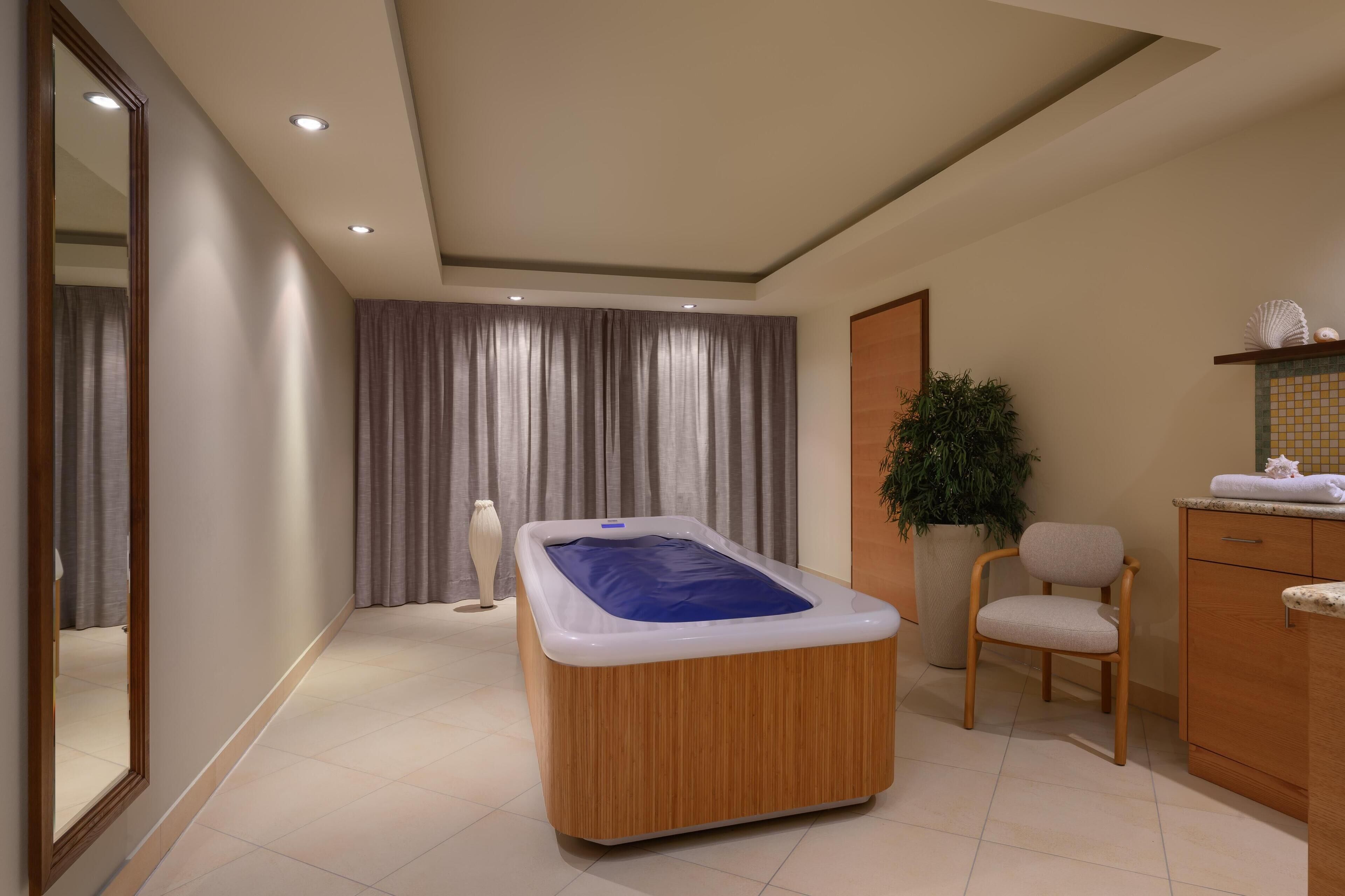A modern bathroom with a wooden bathtub, a sink, a chair, and a potted plant.
