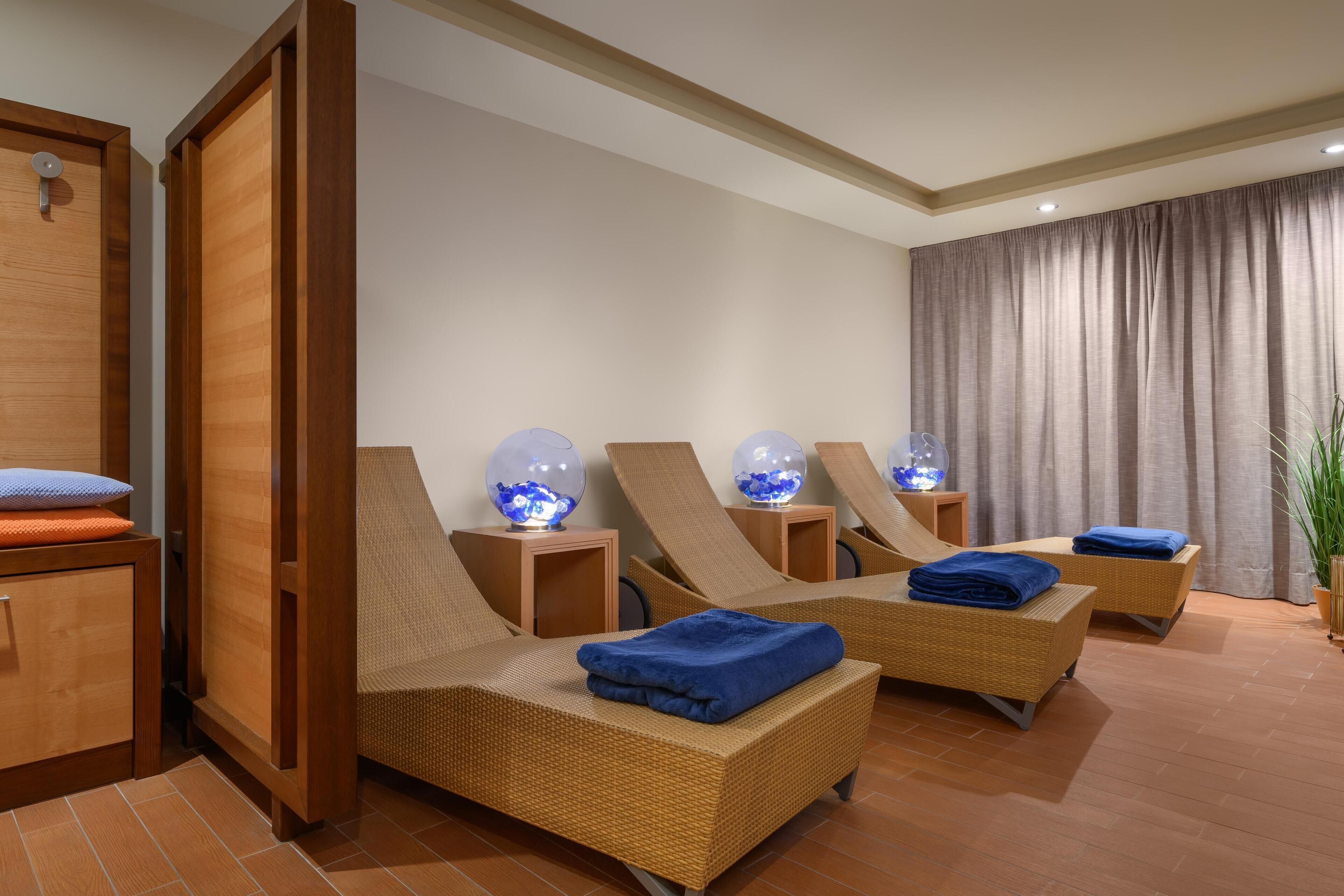 Ein Spa-Raum mit drei Korbsesseln, jeweils mit blauem Handtuch und einer Glaskugel-Lampe.