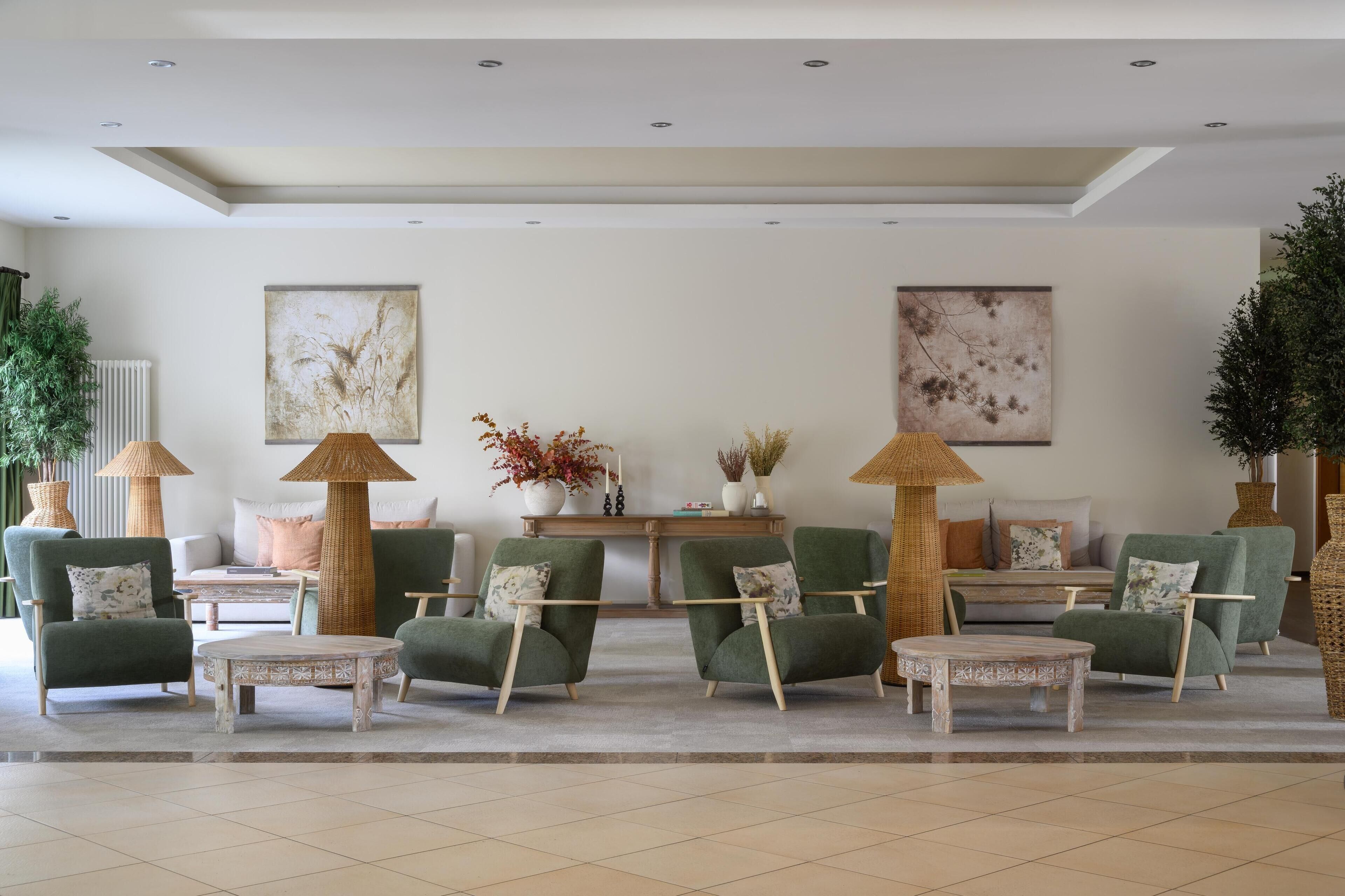 A modern lobby with green armchairs, round tables, and decorative lamps.