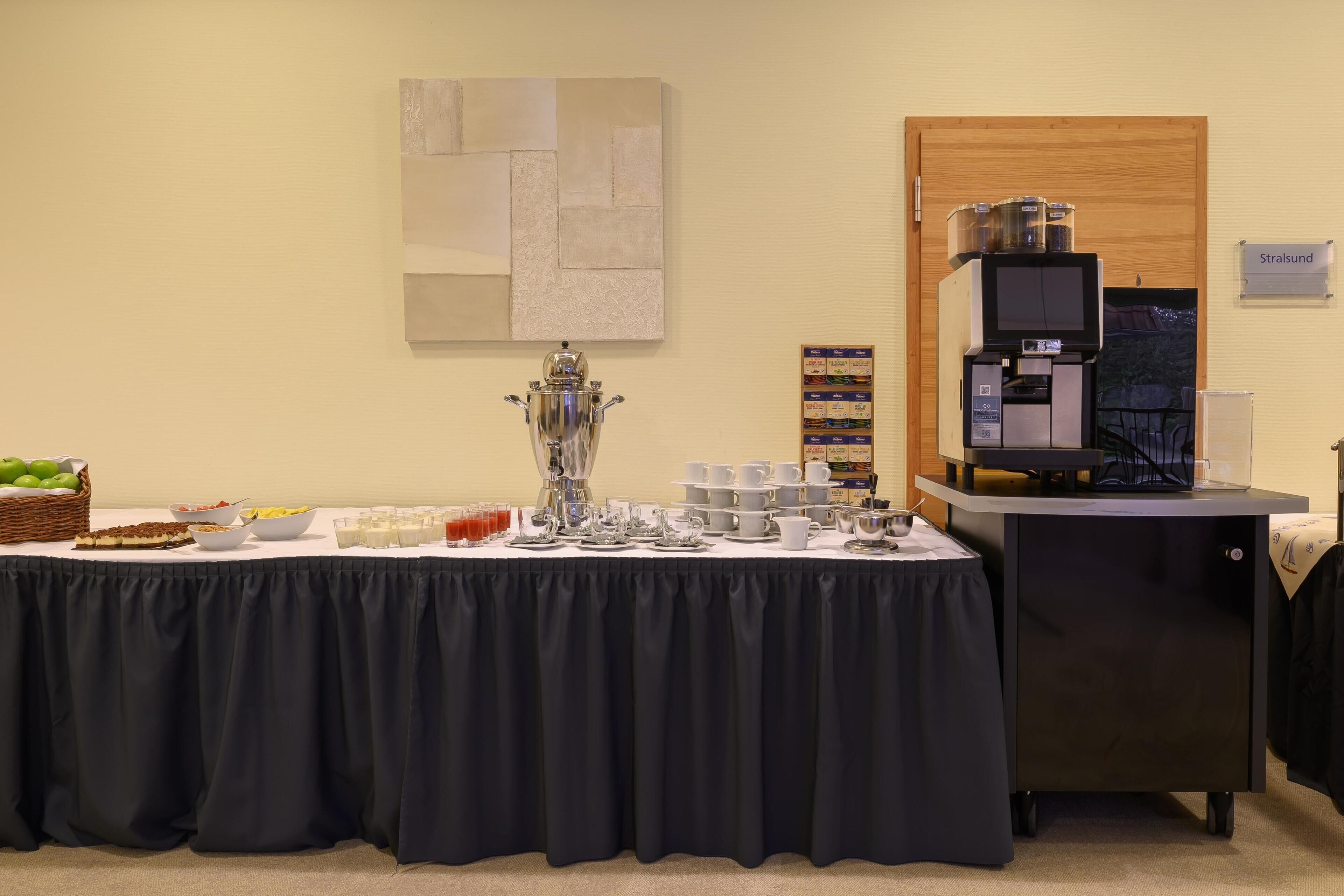 Ein Buffet mit einer Kaffeemaschine, einer großen Dekorvase und verschiedenen Speisen und Getränken.